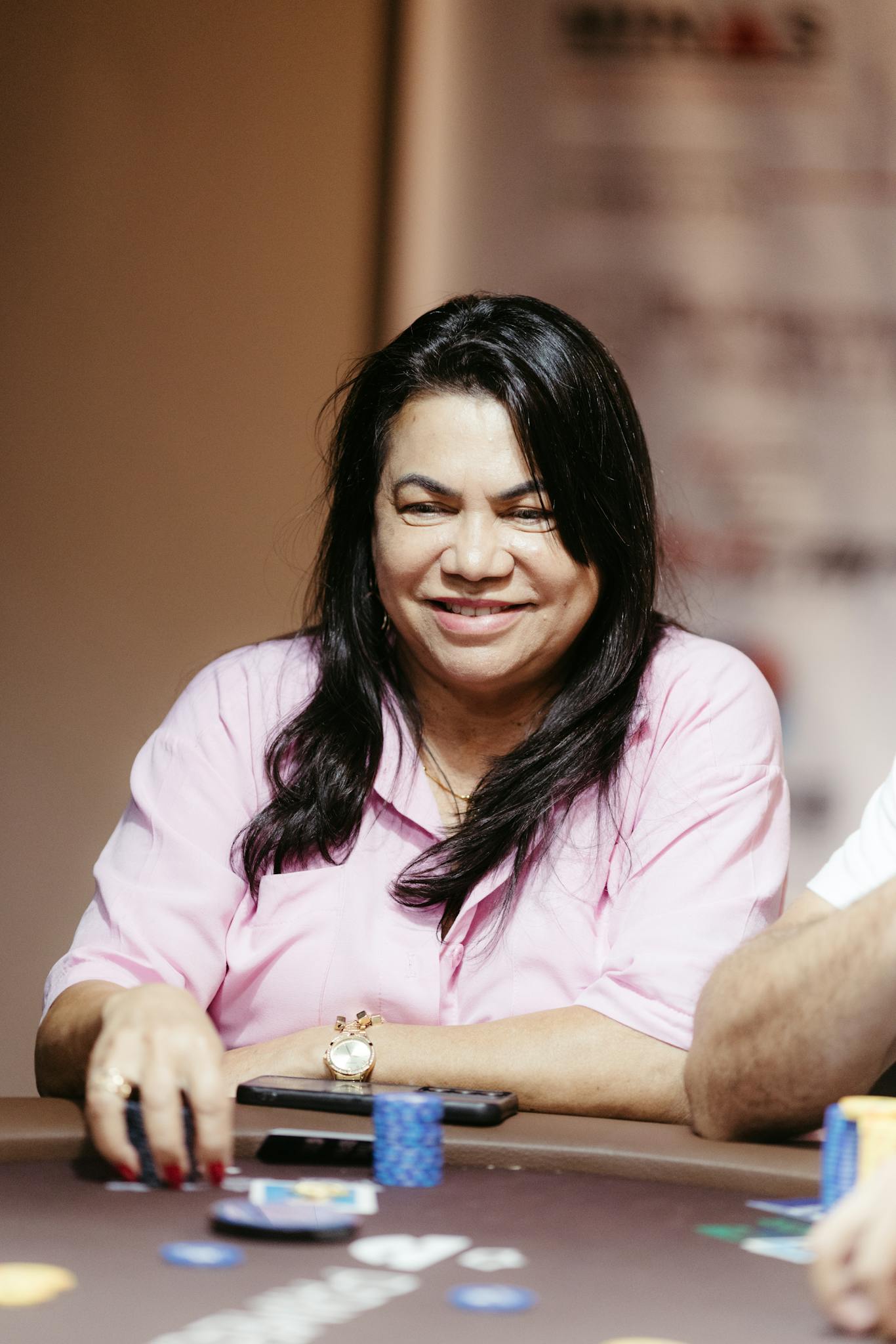 Smiling woman playing poker with chips at a table indoors.